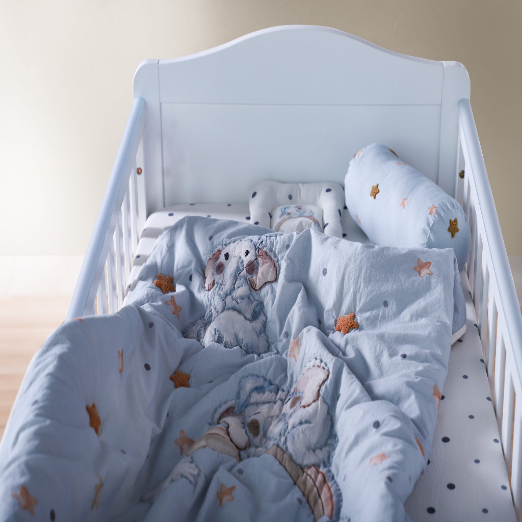 White crib with blue bedding featuring teddy bears and stars on a light wooden floor.