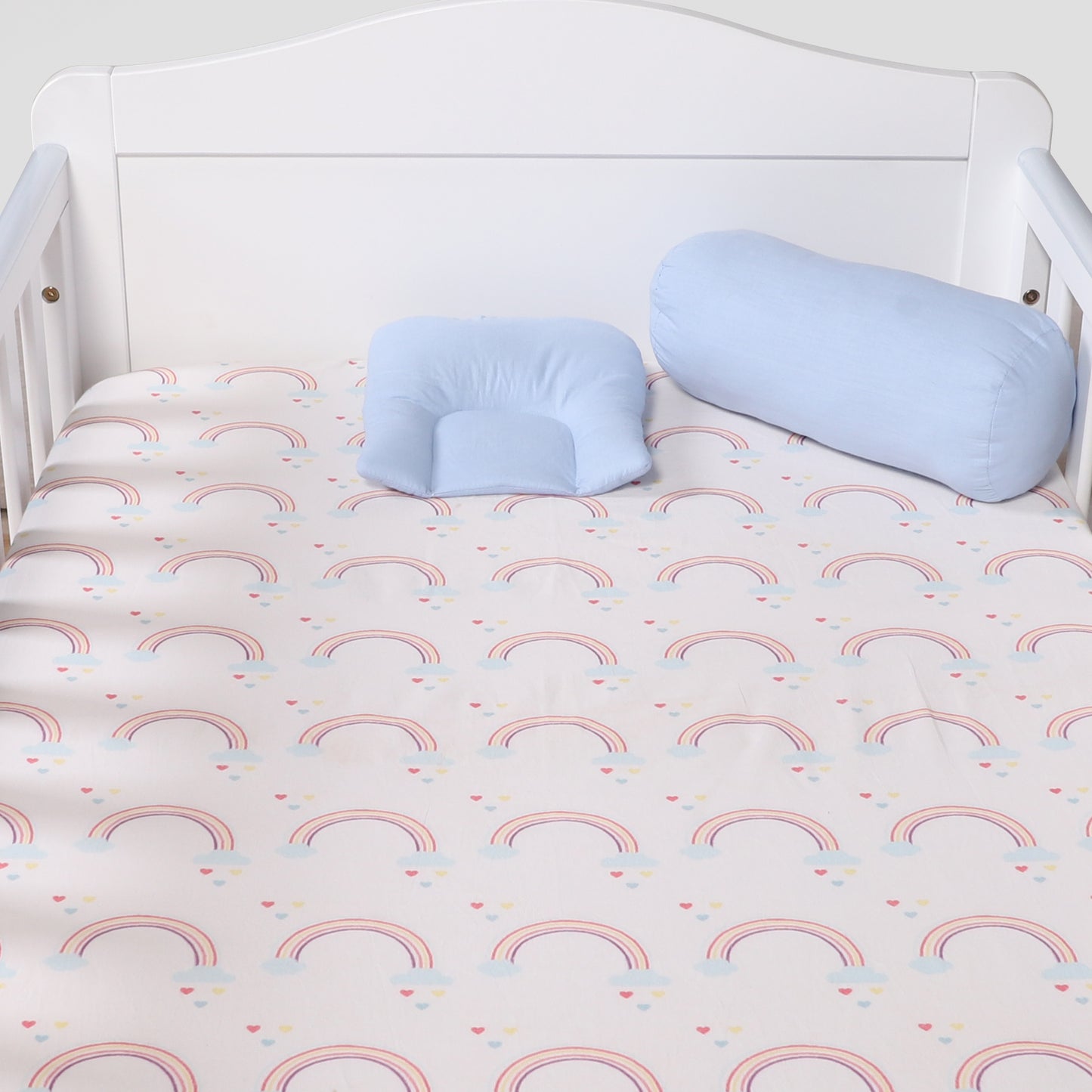 Two blue pillows on a crib with a rainbow-patterned sheet