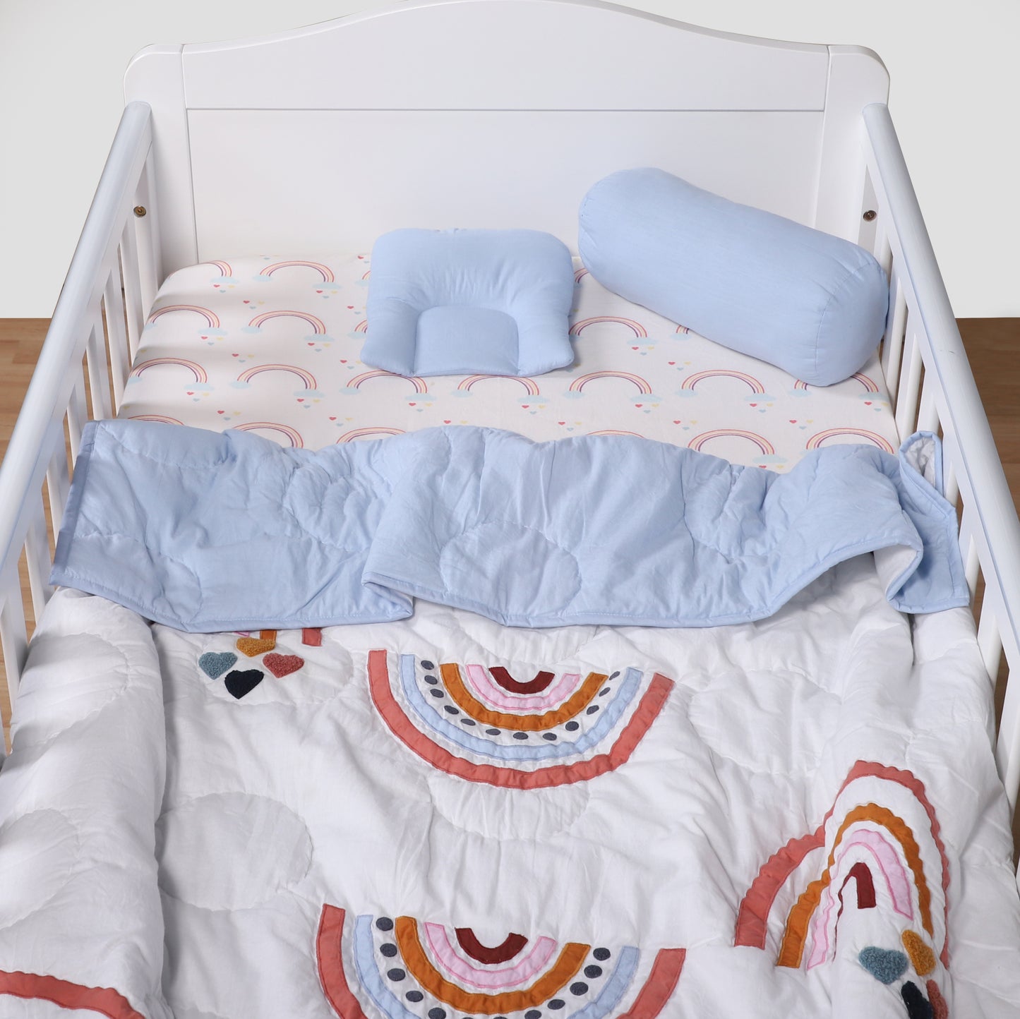 Baby crib with blue bedding and rainbow-patterned quilt
