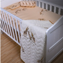 A baby quilt with a central embroidered giraffe design, surrounded by a beige and brown pattern, laid on a white crib.