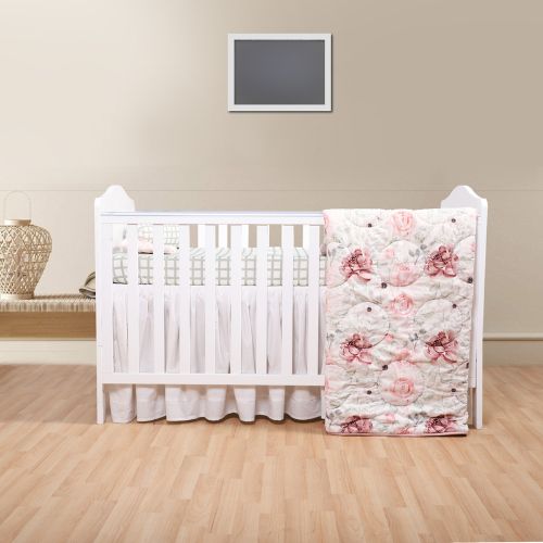 A baby quilt with a floral design in bloom, displayed next to a white crib with a fitted sheet and a bolster pillow, set against a neutral background.