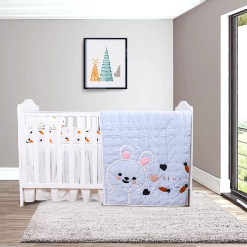A baby quilt with a rabbit design, placed on a crib in a room with a window and decorative curtains.