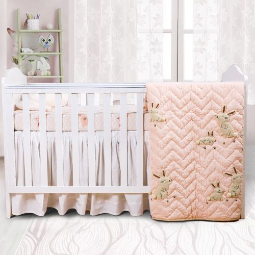A baby quilt with embroidered bunnies on a pink background, displayed next to a crib in a nursery room.