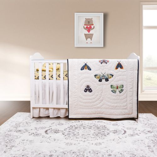 A crib with a white fitted sheet and a Butterfly Biss Baby Quilt with colorful butterfly designs. The crib is set against a light background with a framed picture of a bear above it.