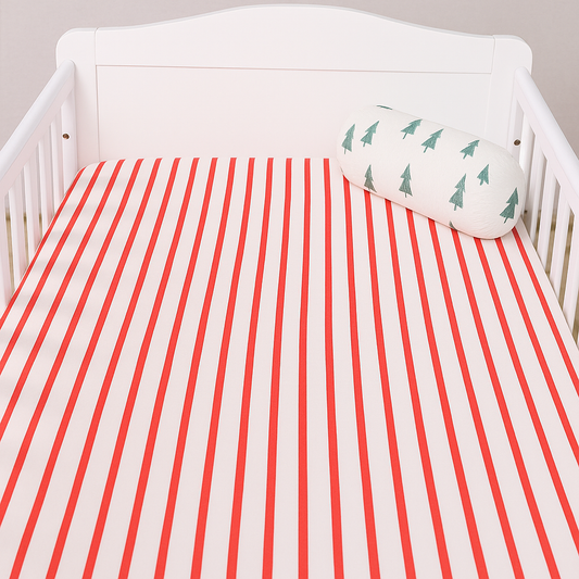 White crib with red and white striped mattress cover and green tree-patterned pillow.