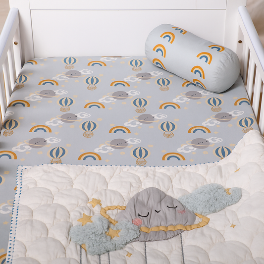 Crib with gray elephant and rainbow patterned mattress cover, white crib bumper, and gray elephant plush toy.