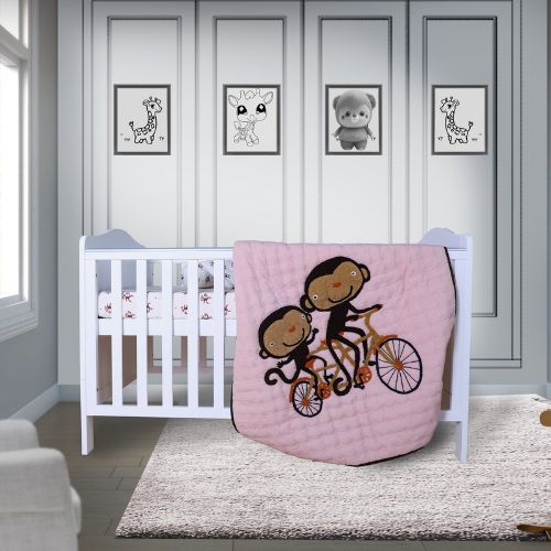 A baby quilt with an embroidered design of two monkeys riding a bicycle, displayed on a crib in a nursery room.