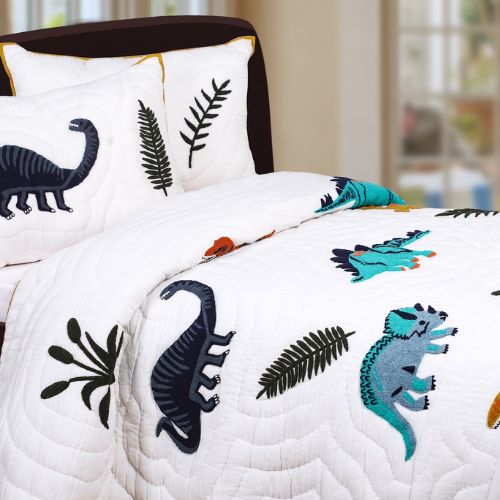 A kids' quilt with dinosaur patterns on a bed, accompanied by pillowcases with matching designs.