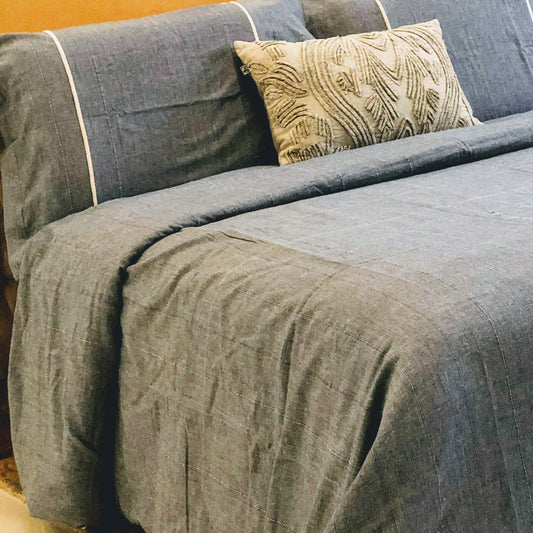 A denim duvet cover in a solid color, displayed on a bed with a decorative pillow on top.