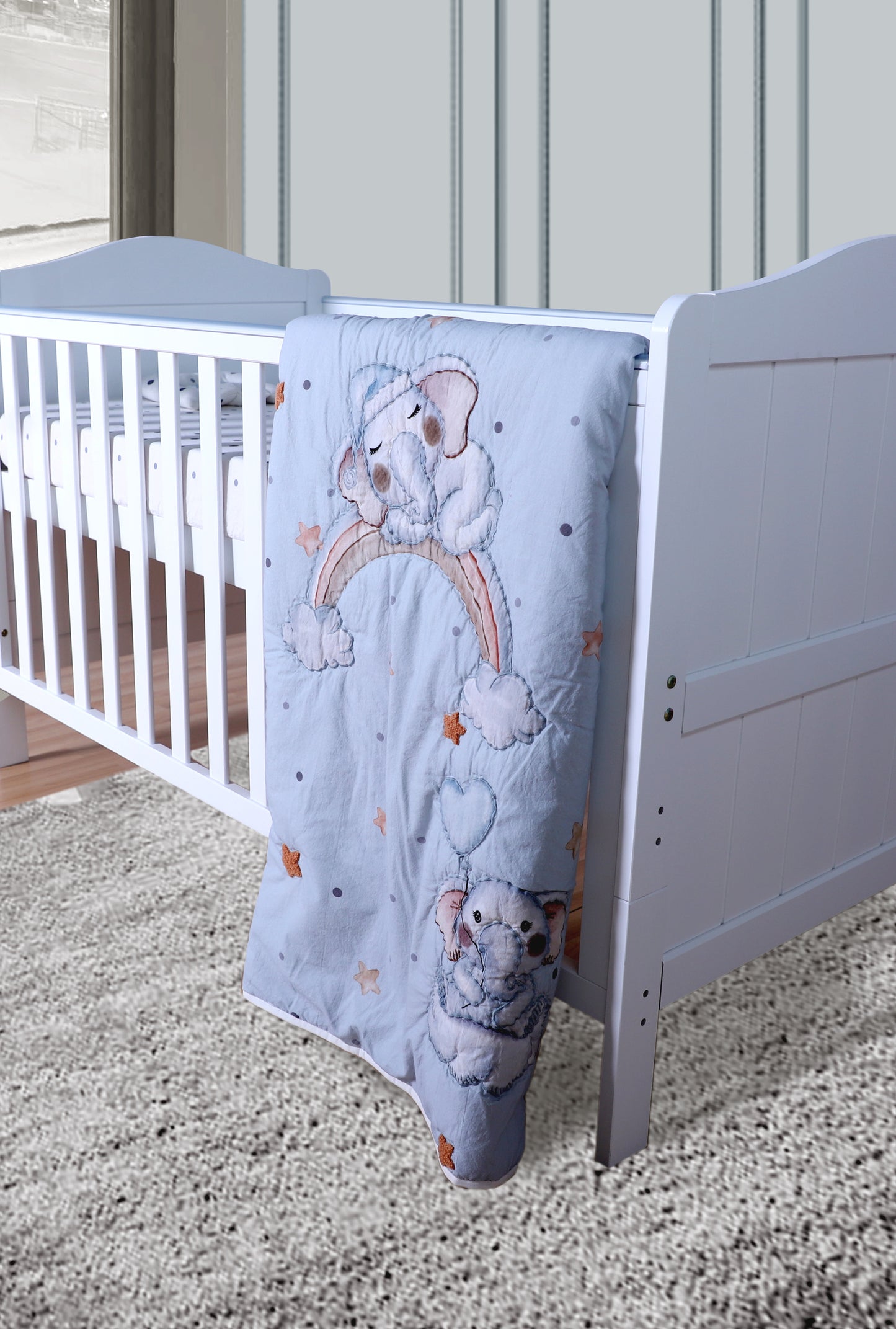 Baby crib with a gray blanket featuring teddy bear designs on a carpeted floor.