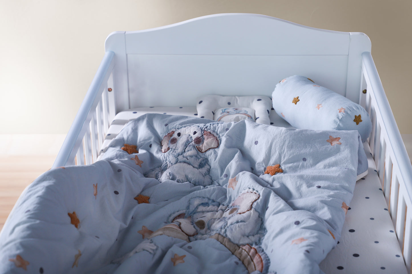 White crib with blue bedding featuring teddy bears and stars on a light wooden floor.