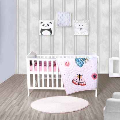 A baby crib set with a quilt featuring butterflies, placed in a nursery room with decorative wall art and a round white rug on the floor.