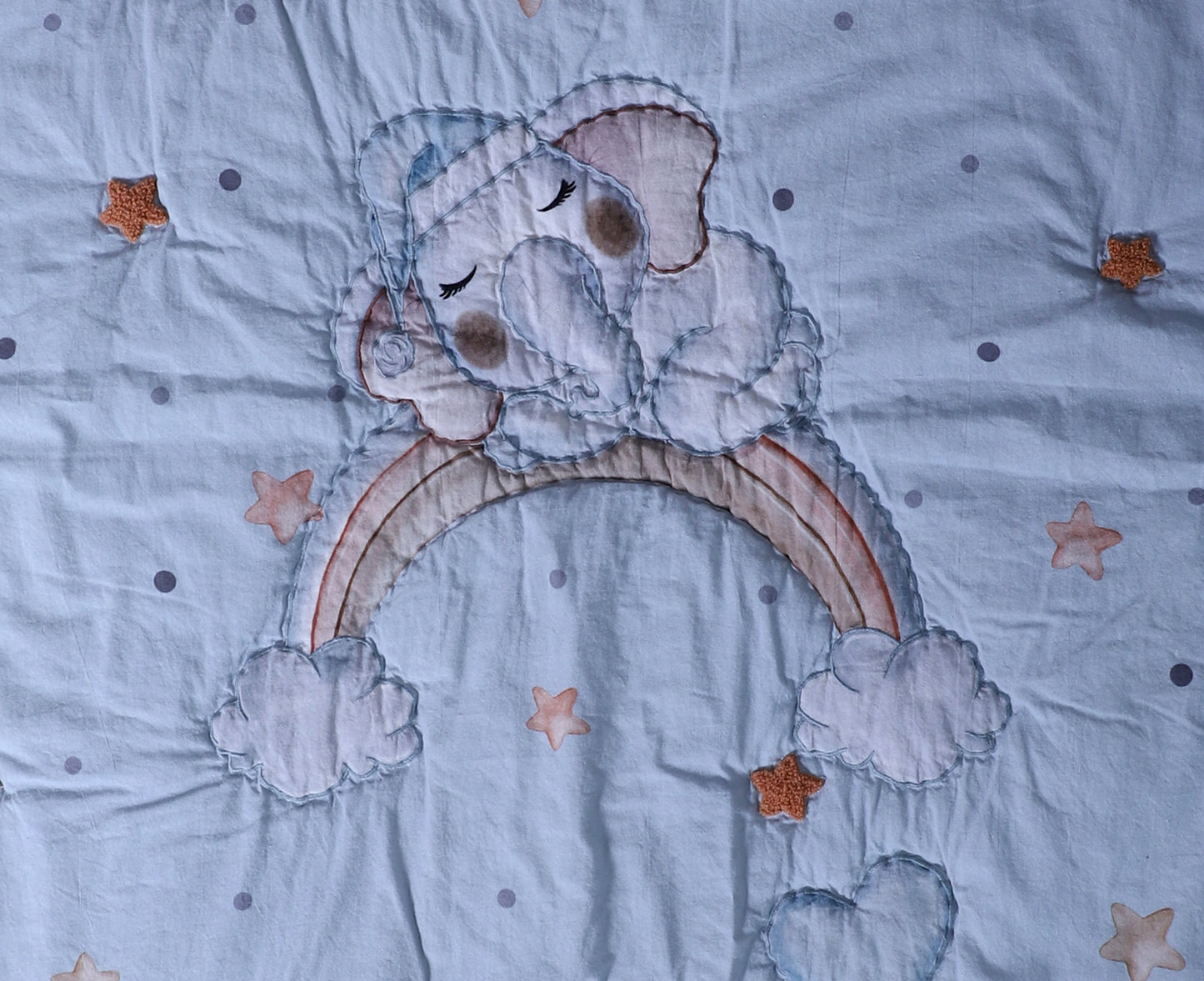 Embroidered design of a bear holding a rainbow on a fabric background with stars.
