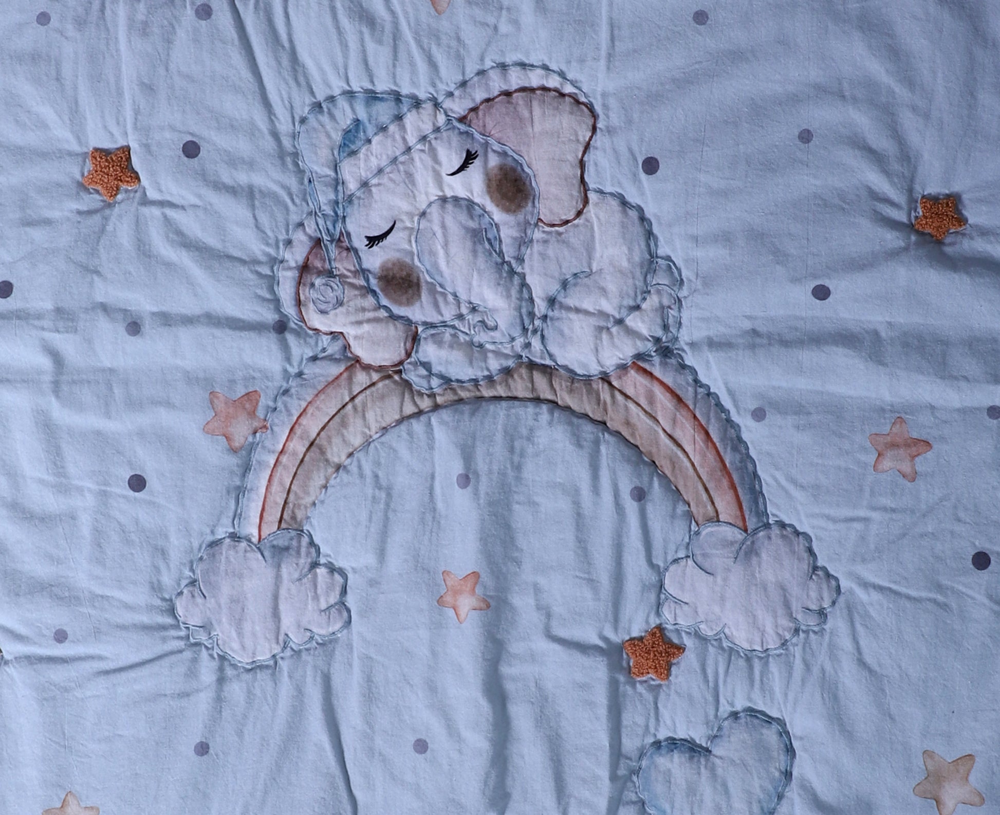 Embroidered design of a bear holding a rainbow on a fabric background with stars.