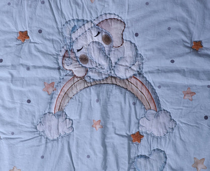 Embroidered design of a bear holding a rainbow on a fabric background with stars.