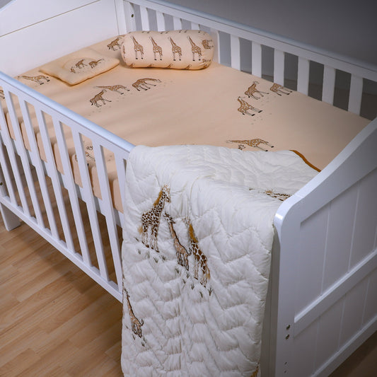 White crib with beige and white quilt featuring giraffe patterns on a wooden floor.
