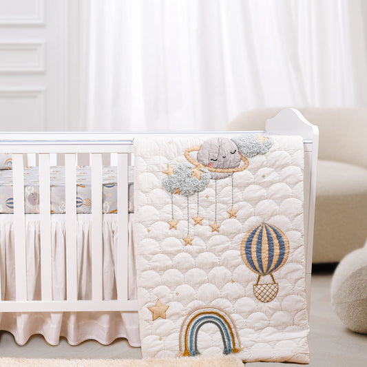 A baby crib set with a quilt featuring rainbow and whimsical animal character designs, along with a fitted sheet and a baby pillow.