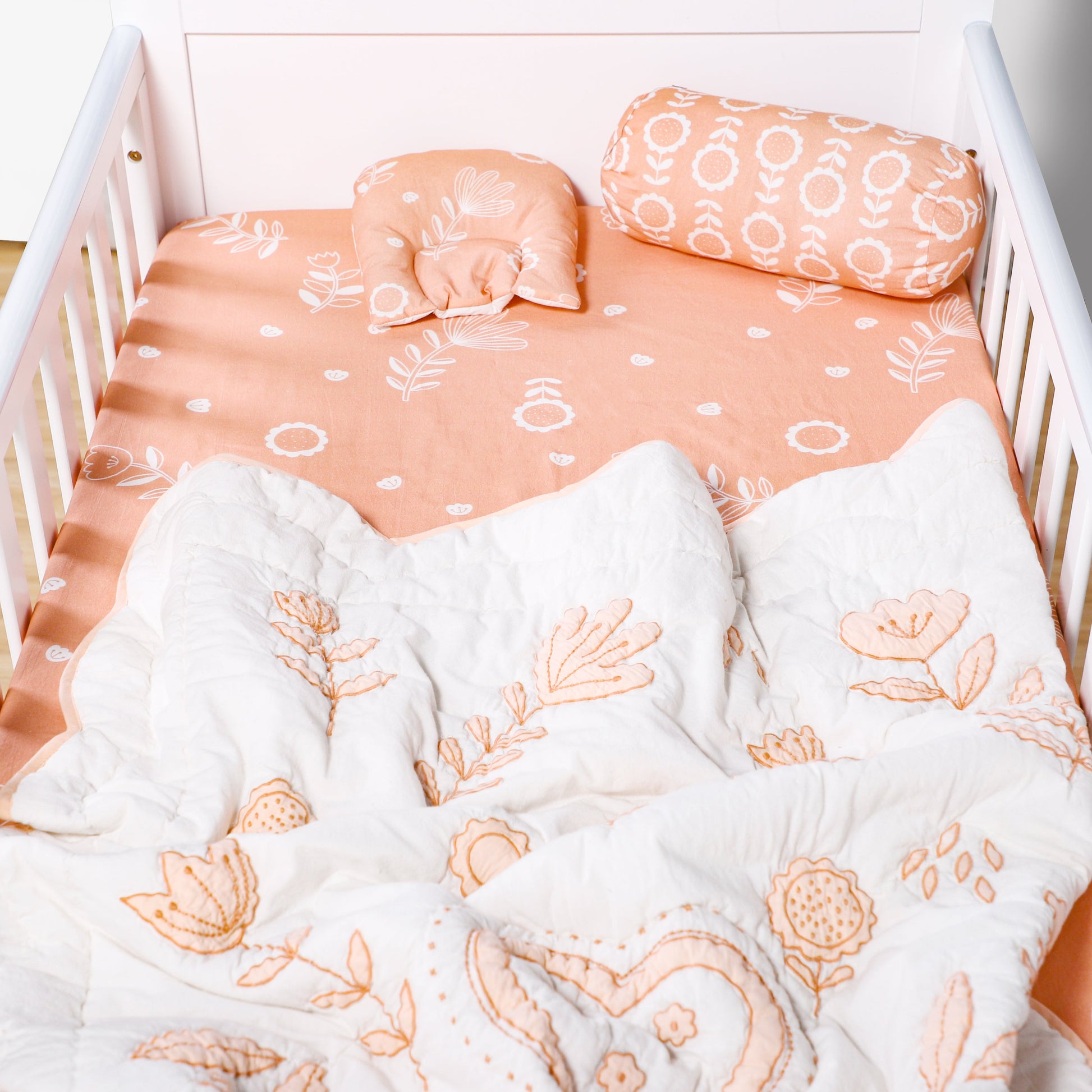Crib with floral bedding and pillows in a soft peach color scheme.