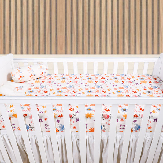 White crib with colorful floral bumper pad against a wooden wall.
