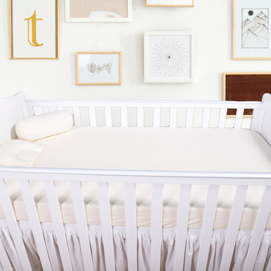 White crib with white bedding in a room with framed pictures on the wall.