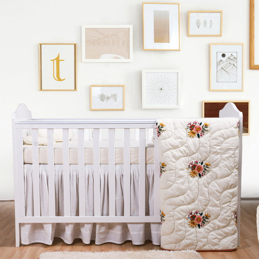Nursery room with a white crib and floral quilt against a wall with framed pictures.