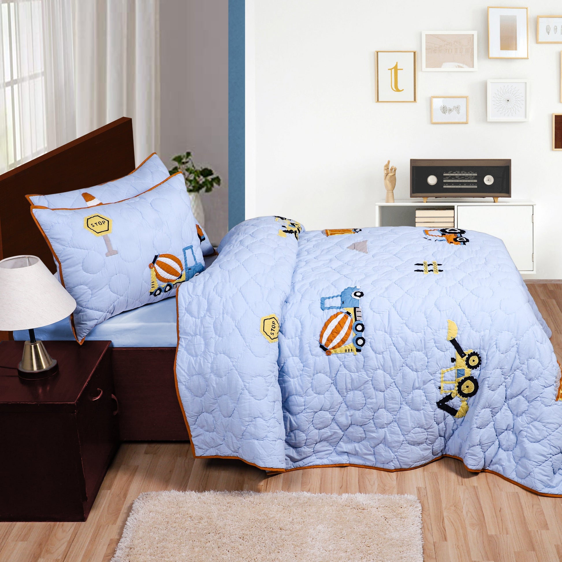 Light blue quilt with cartoon designs on a bed in a room with furniture and decor.