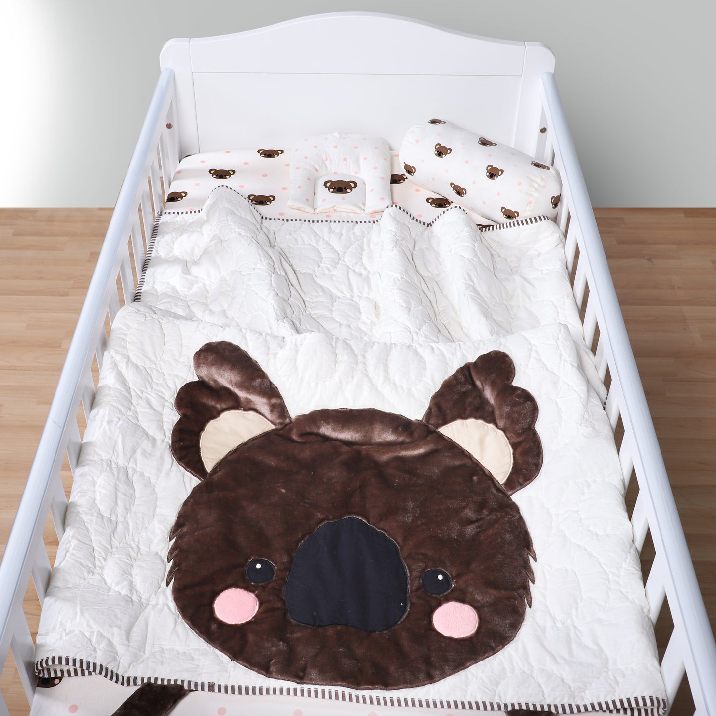 Crib with brown bear-shaped pillow and white crib sheet on a wooden floor.