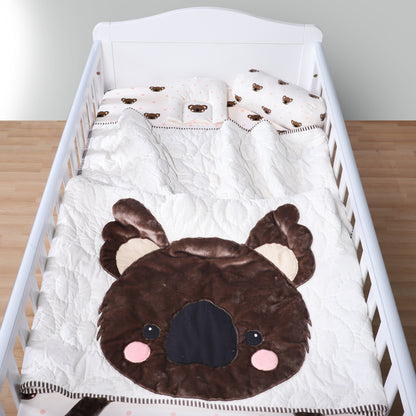Crib with brown bear-shaped pillow and white crib sheet on a wooden floor.