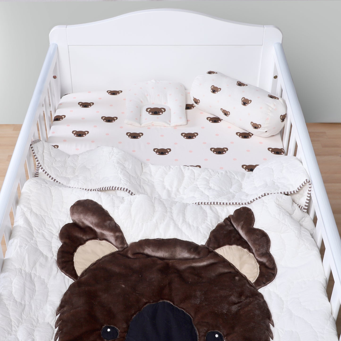 Baby crib with brown bear-themed bedding and pillows.