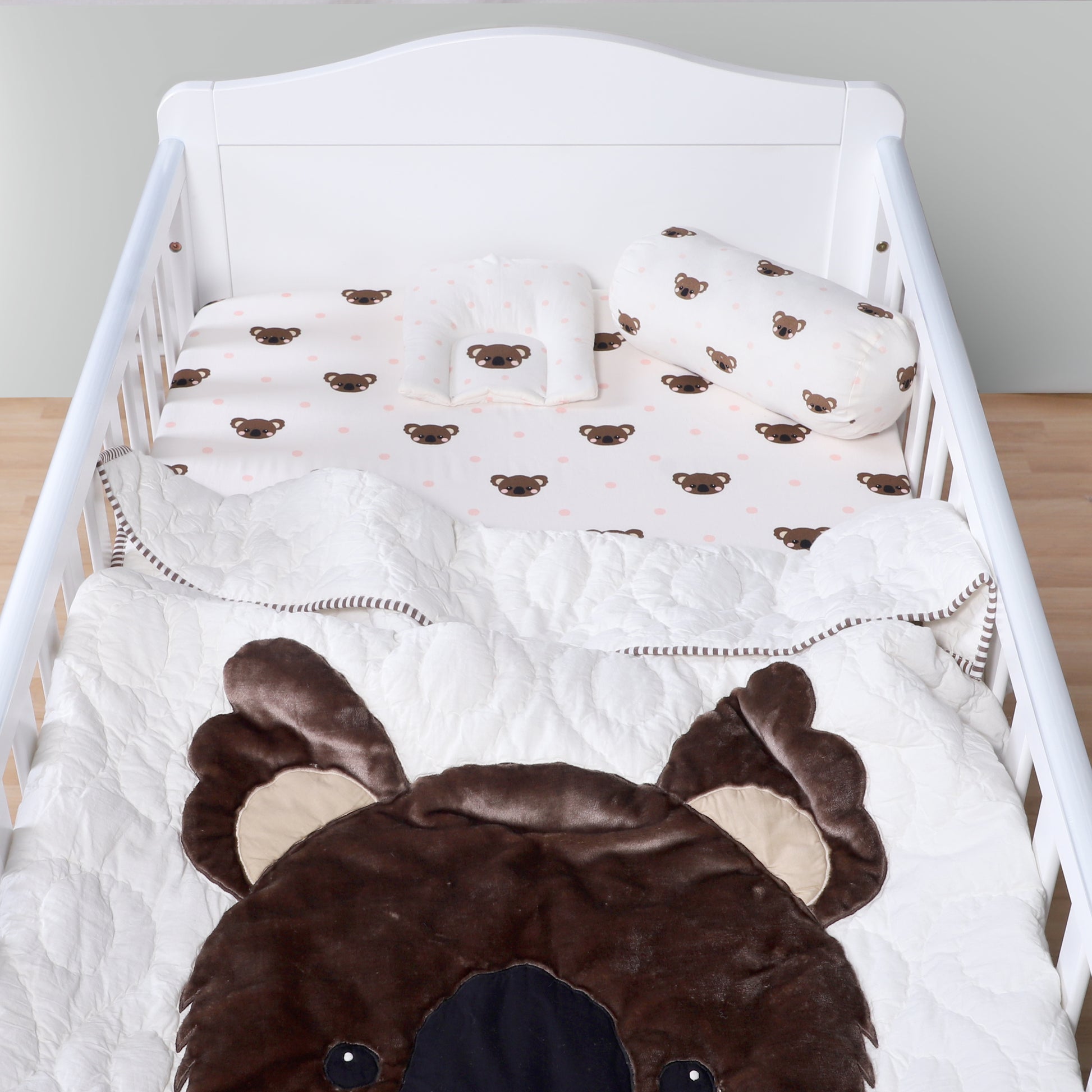 Baby crib with brown bear-themed bedding and pillows.