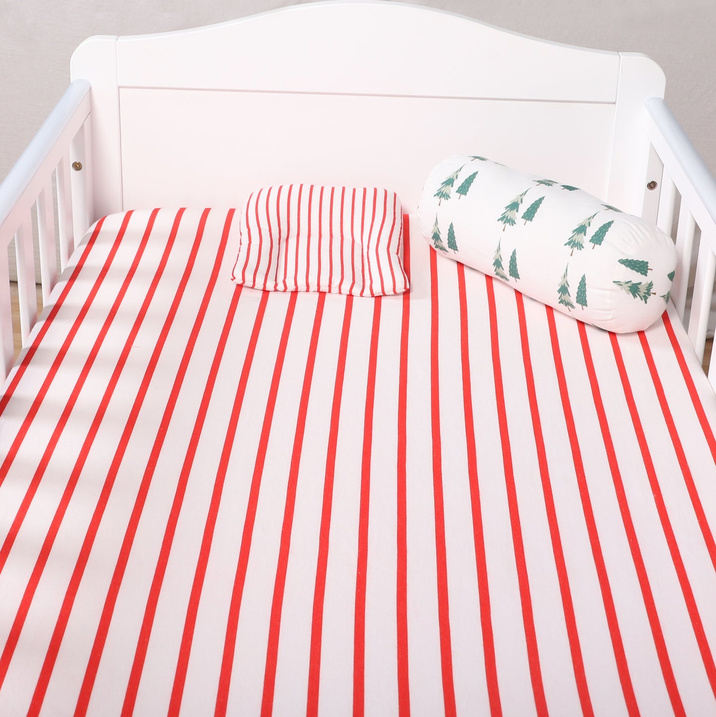 Crib with red and white striped bedding and a green patterned pillow.
