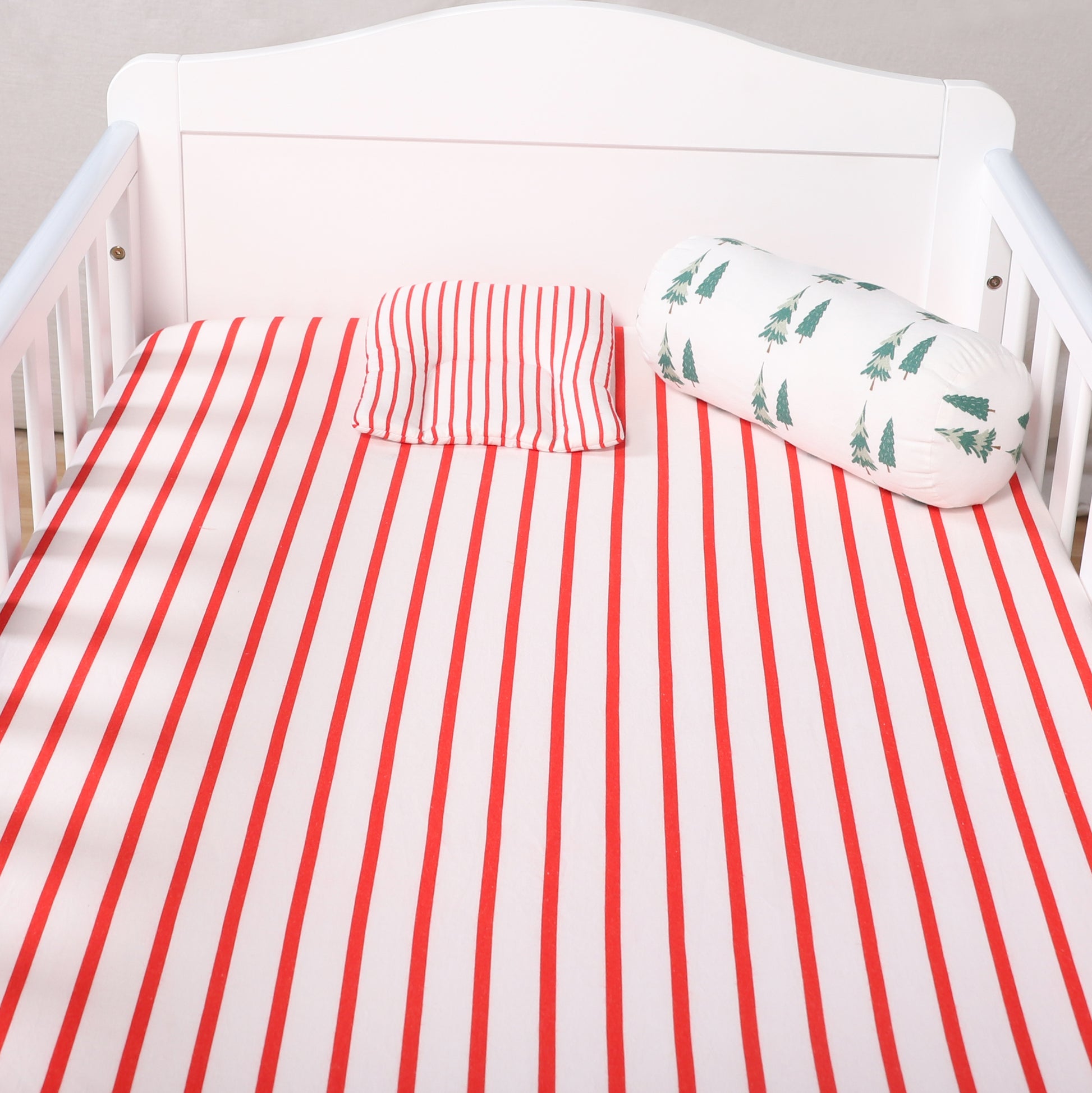 Crib with red and white striped bedding and a green patterned pillow.