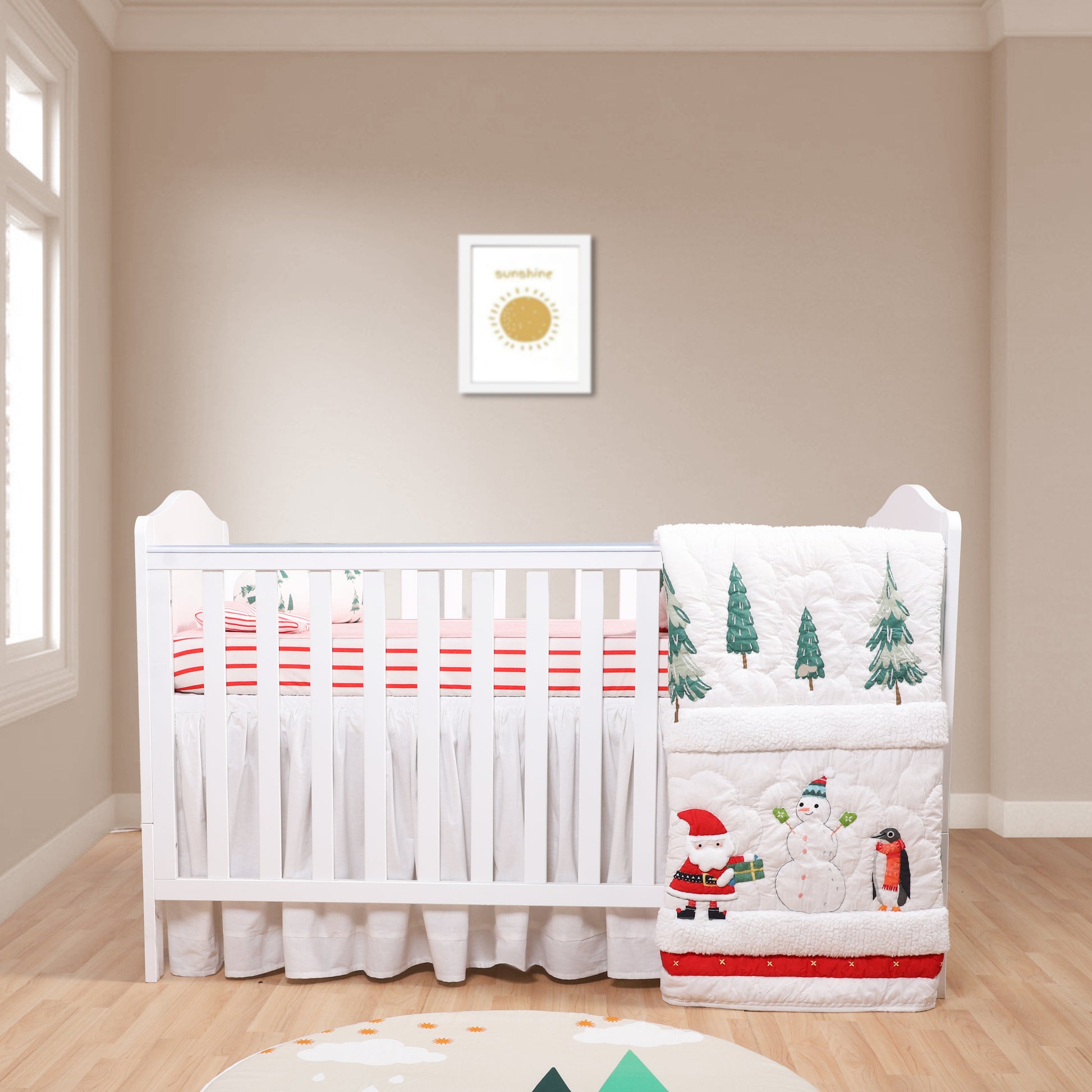 Baby crib with festive bedding featuring Santa, snowman, and penguin in a room with a framed picture on the wall.