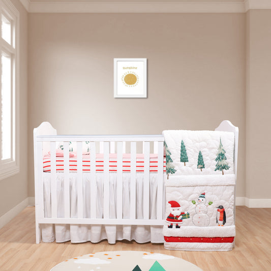 Baby crib with festive bedding featuring Santa, snowman, and penguin in a room with a framed picture on the wall.