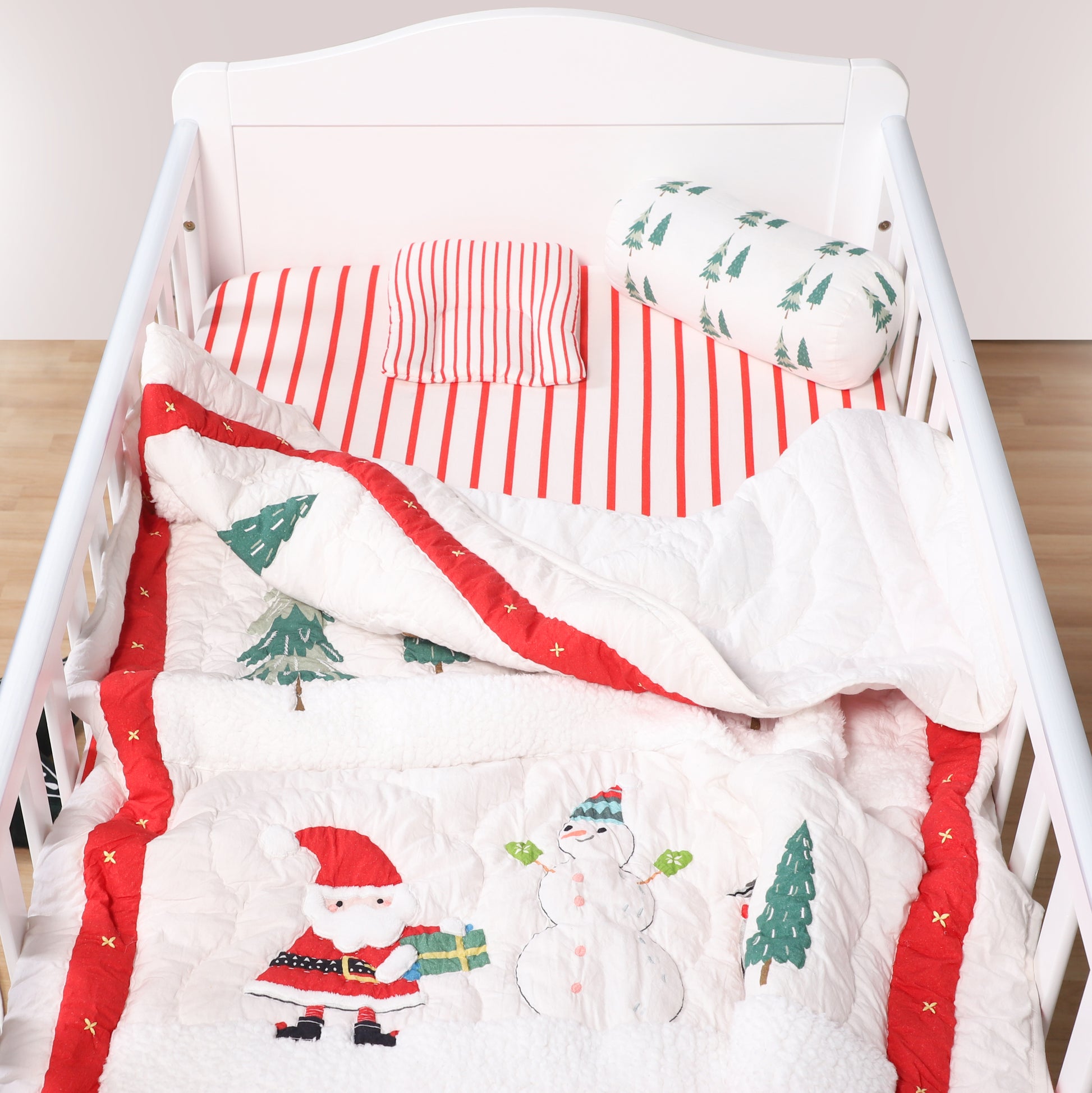 Baby crib with Christmas-themed bedding featuring Santa Claus and a snowman.
