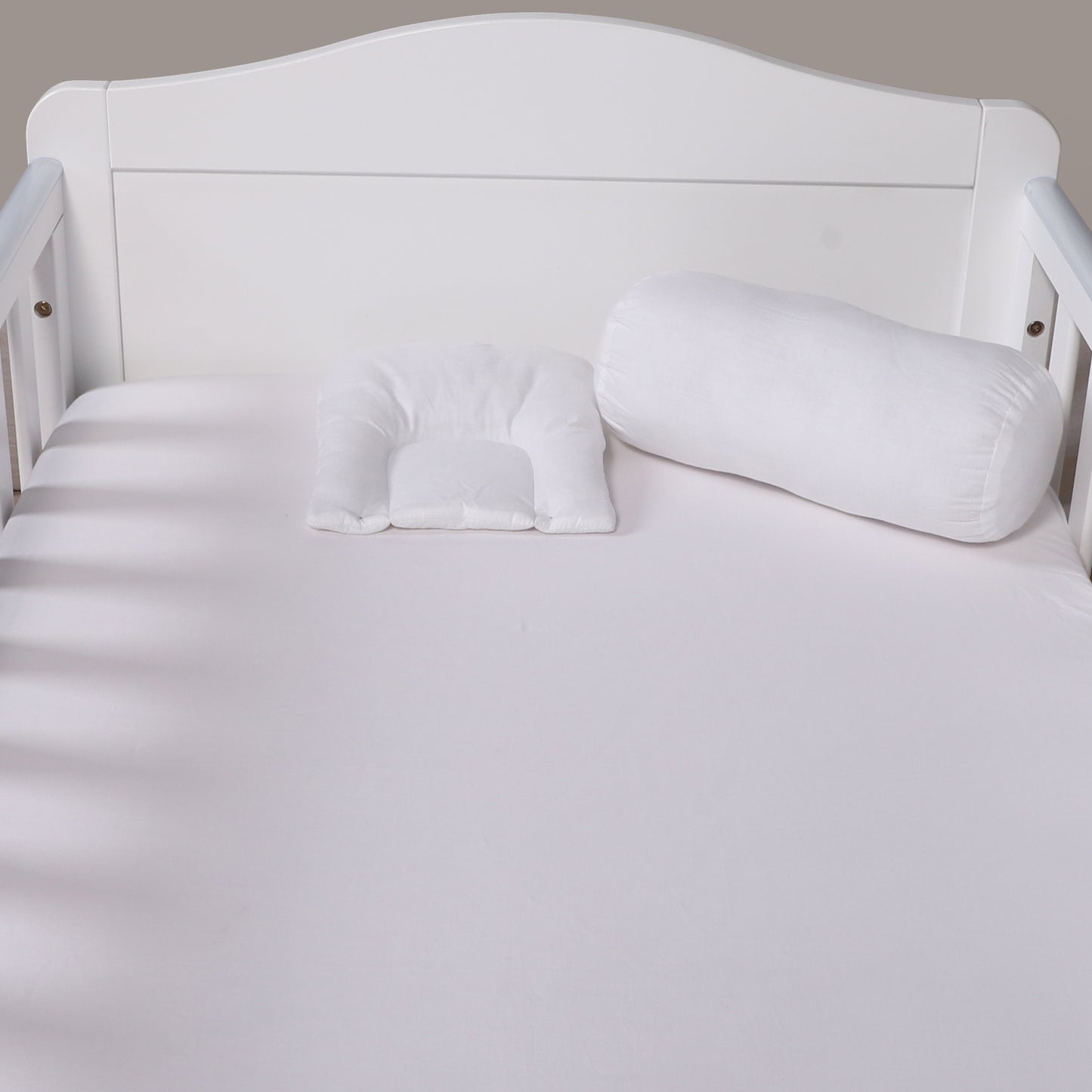 White U-shaped body pillow on a white bed with a neutral headboard.