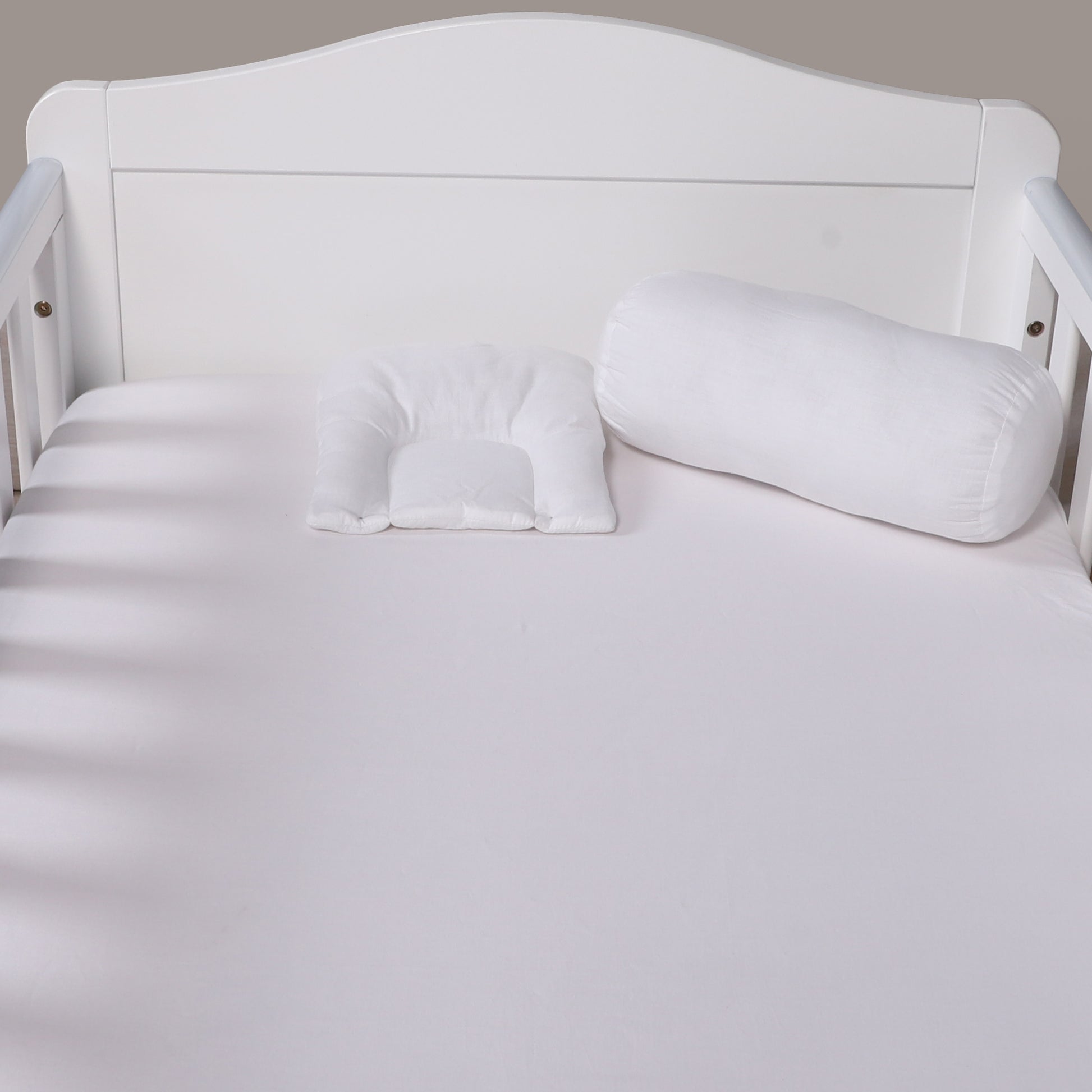 White U-shaped body pillow on a white bed with a neutral headboard.