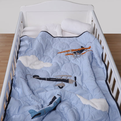 Crib with a blue quilt featuring airplane designs on a wooden floor.