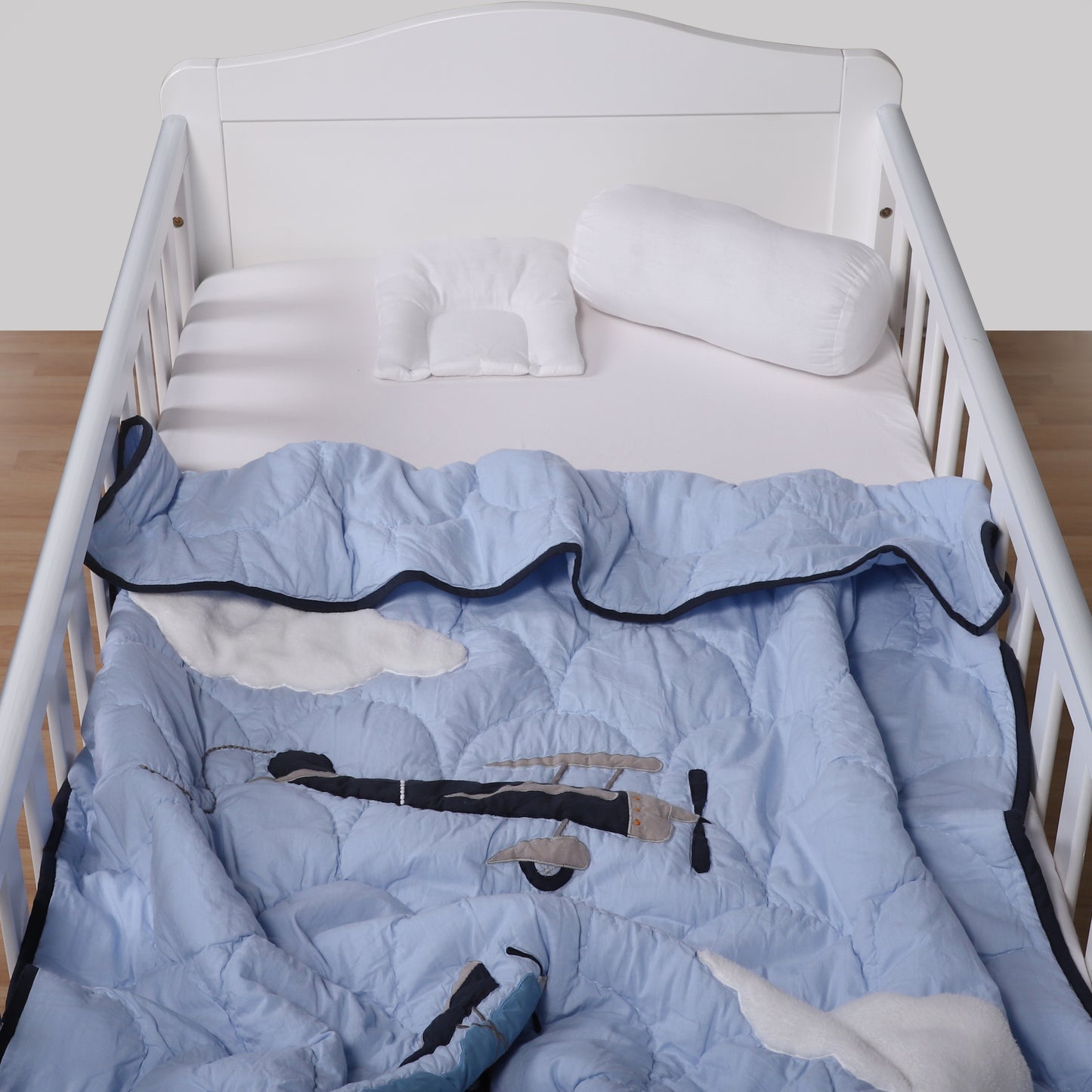 White crib with blue quilt featuring cartoon characters on a wooden floor.
