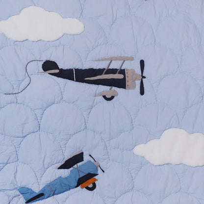 Quilt with airplane and skier design against a blue sky with clouds
