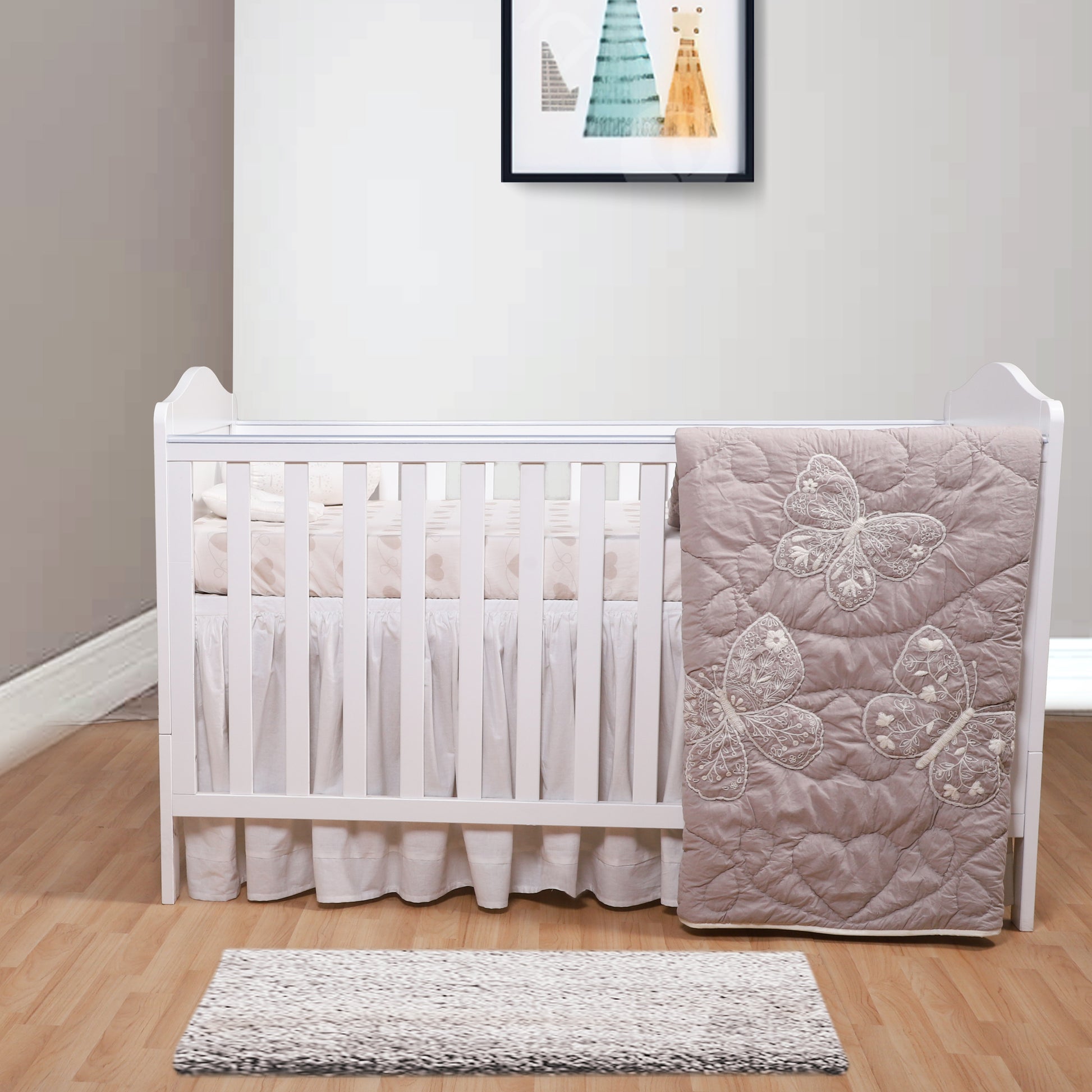 White crib with pink butterfly-patterned blanket in a room with a rug and wall art.