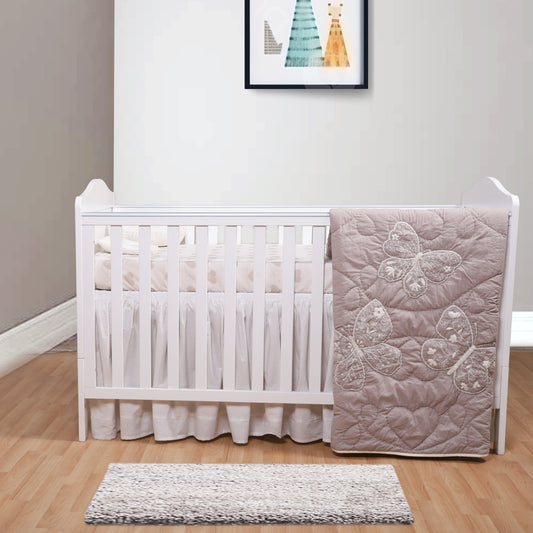 White crib with pink butterfly-patterned blanket in a room with a rug and wall art.