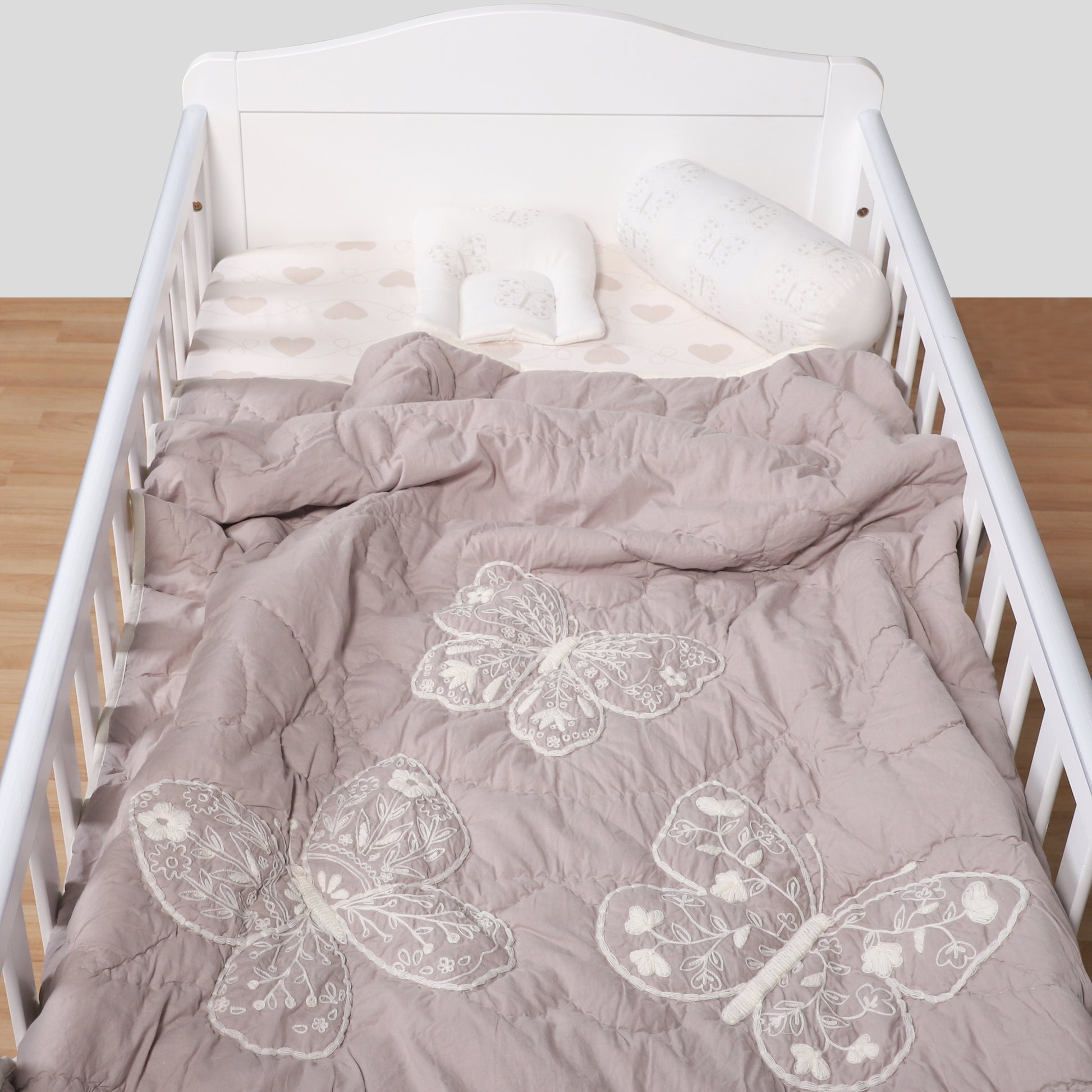 Crib with gray butterfly-patterned bedding on a wooden floor.