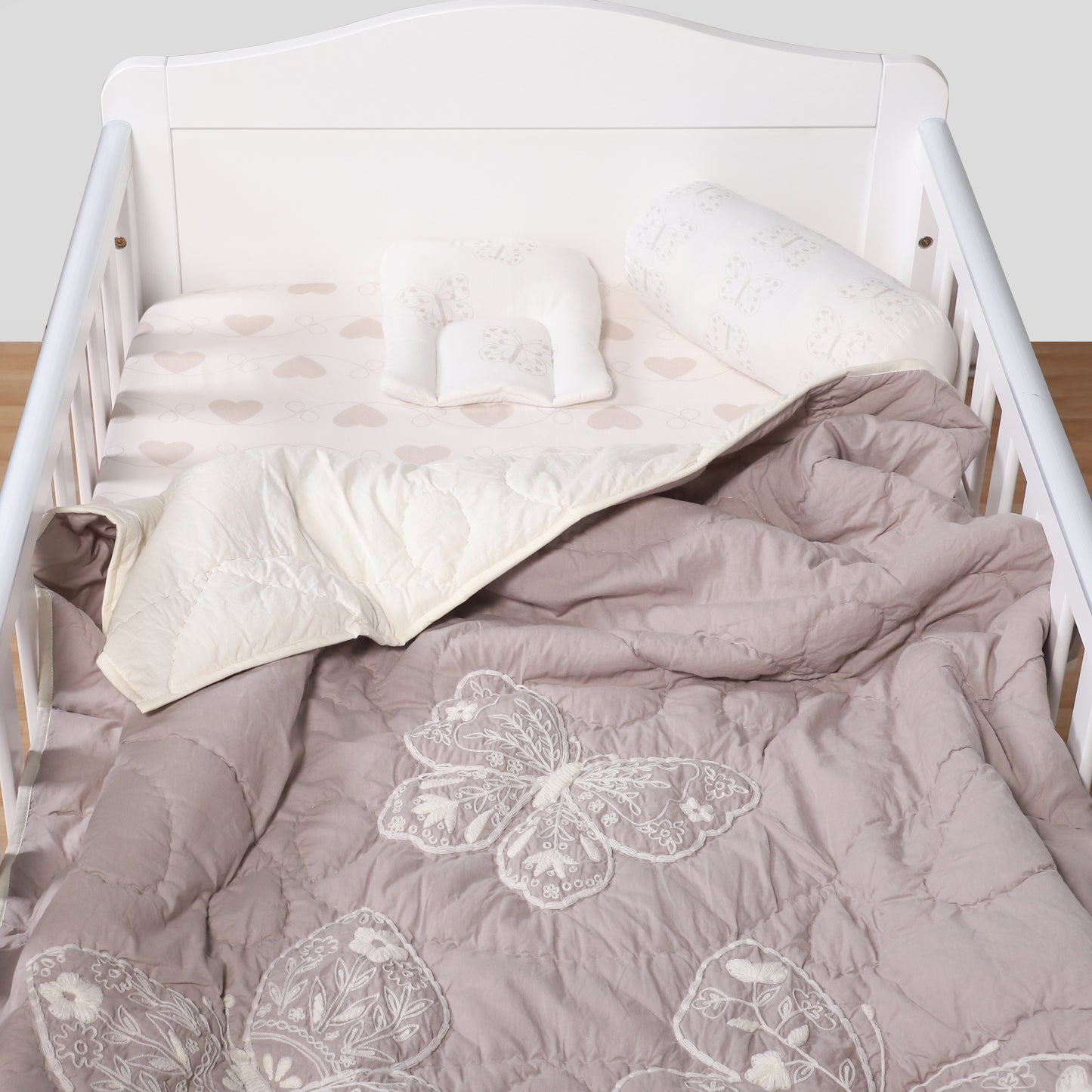 White crib with gray comforter featuring butterfly designs on a plain background
