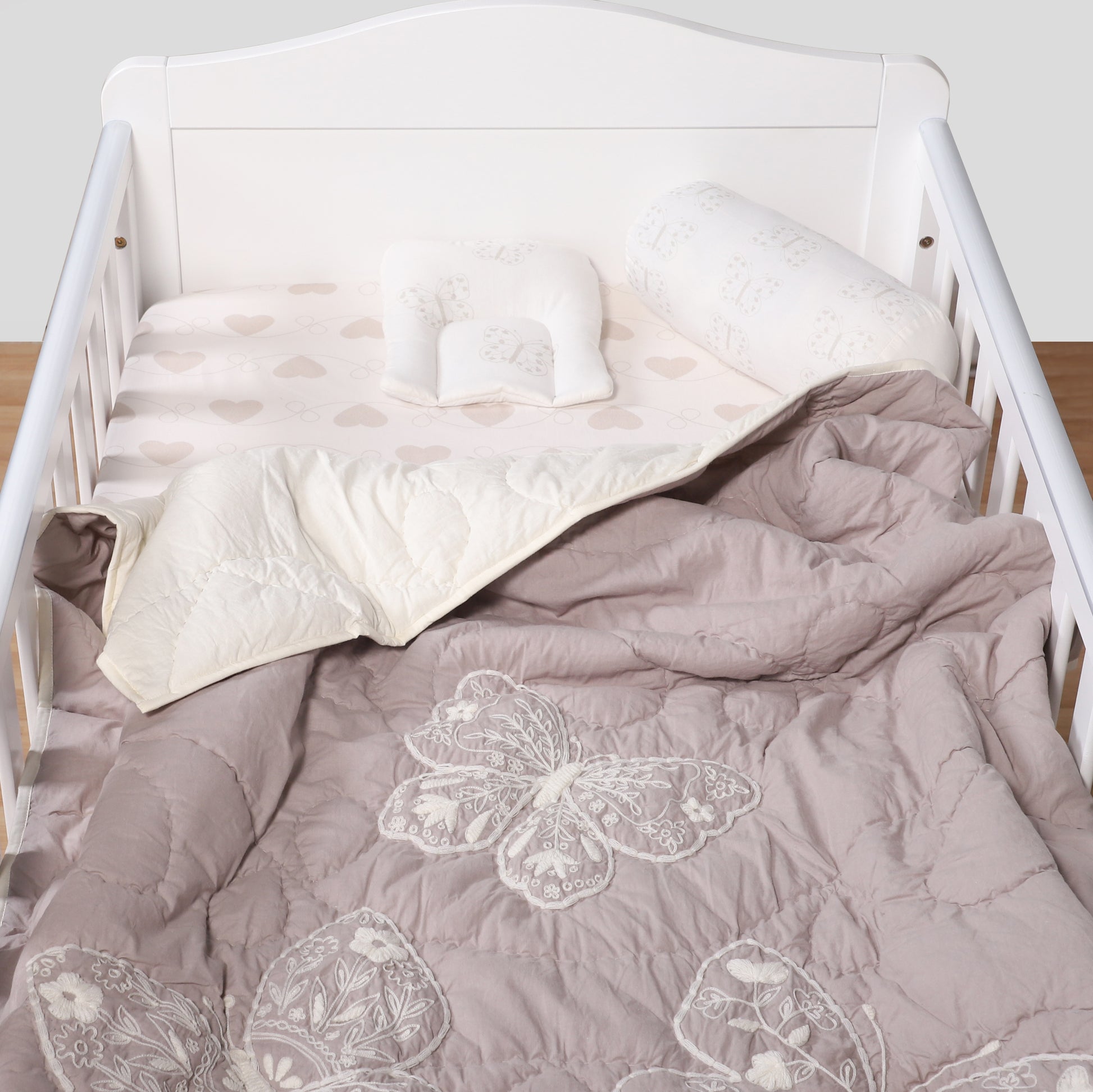 White crib with gray comforter featuring butterfly designs on a plain background