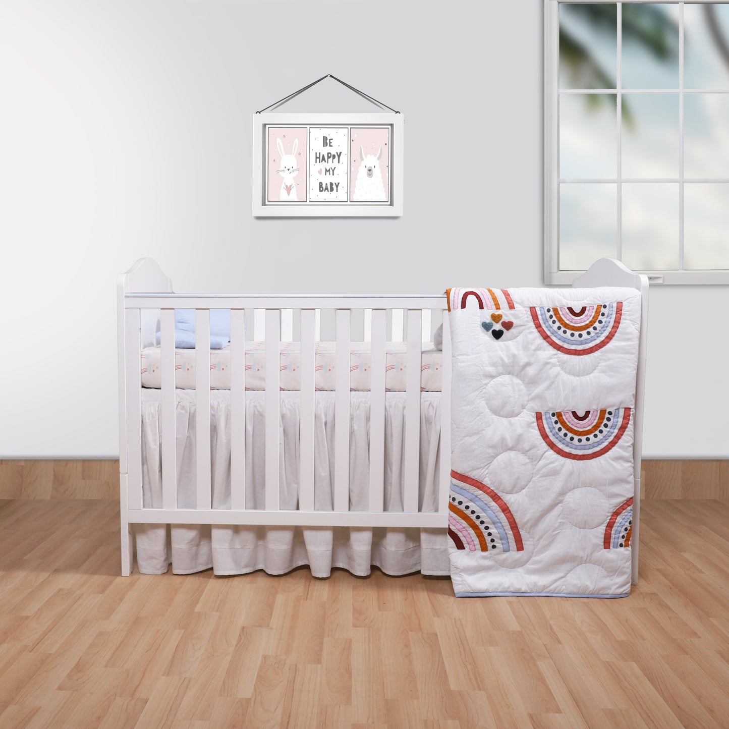 Nursery room with a crib and rainbow-patterned quilt on a wooden floor.