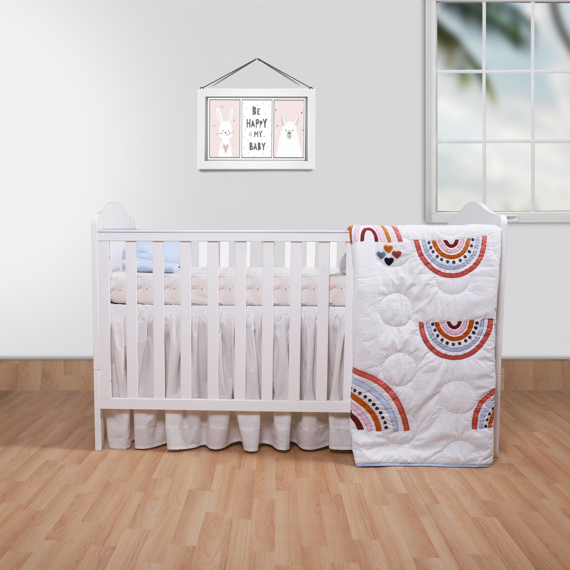 Nursery room with a crib and rainbow-patterned quilt on a wooden floor.