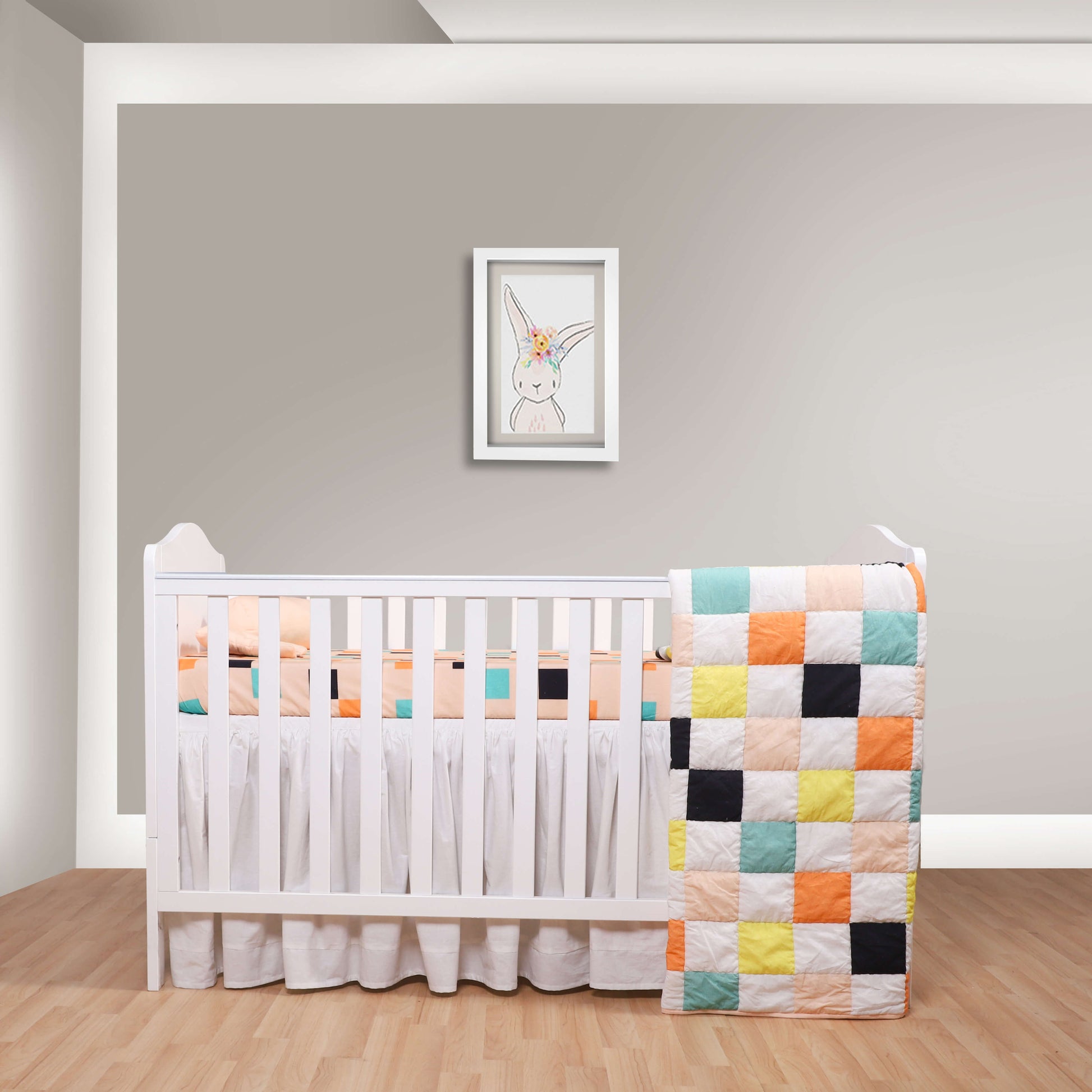 A baby quilt with a vibrant checkered pattern displayed on a crib in a nursery room.