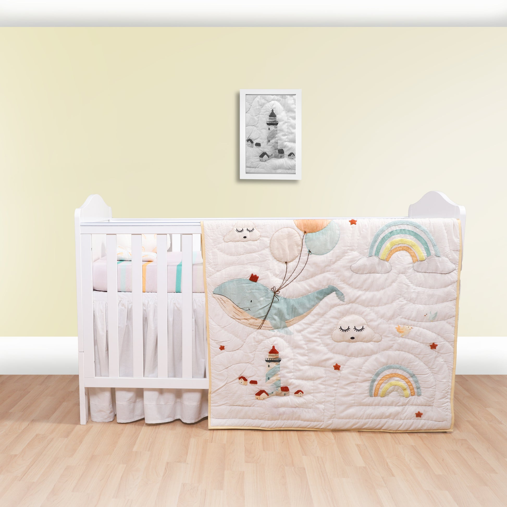 Crib with a decorative quilt featuring cartoon whales and rainbows against a light yellow wall.