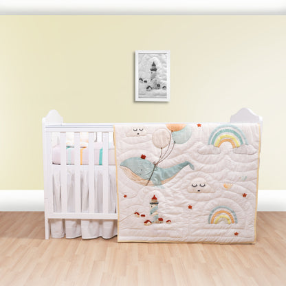 Crib with a decorative quilt featuring cartoon whales and rainbows against a light yellow wall.